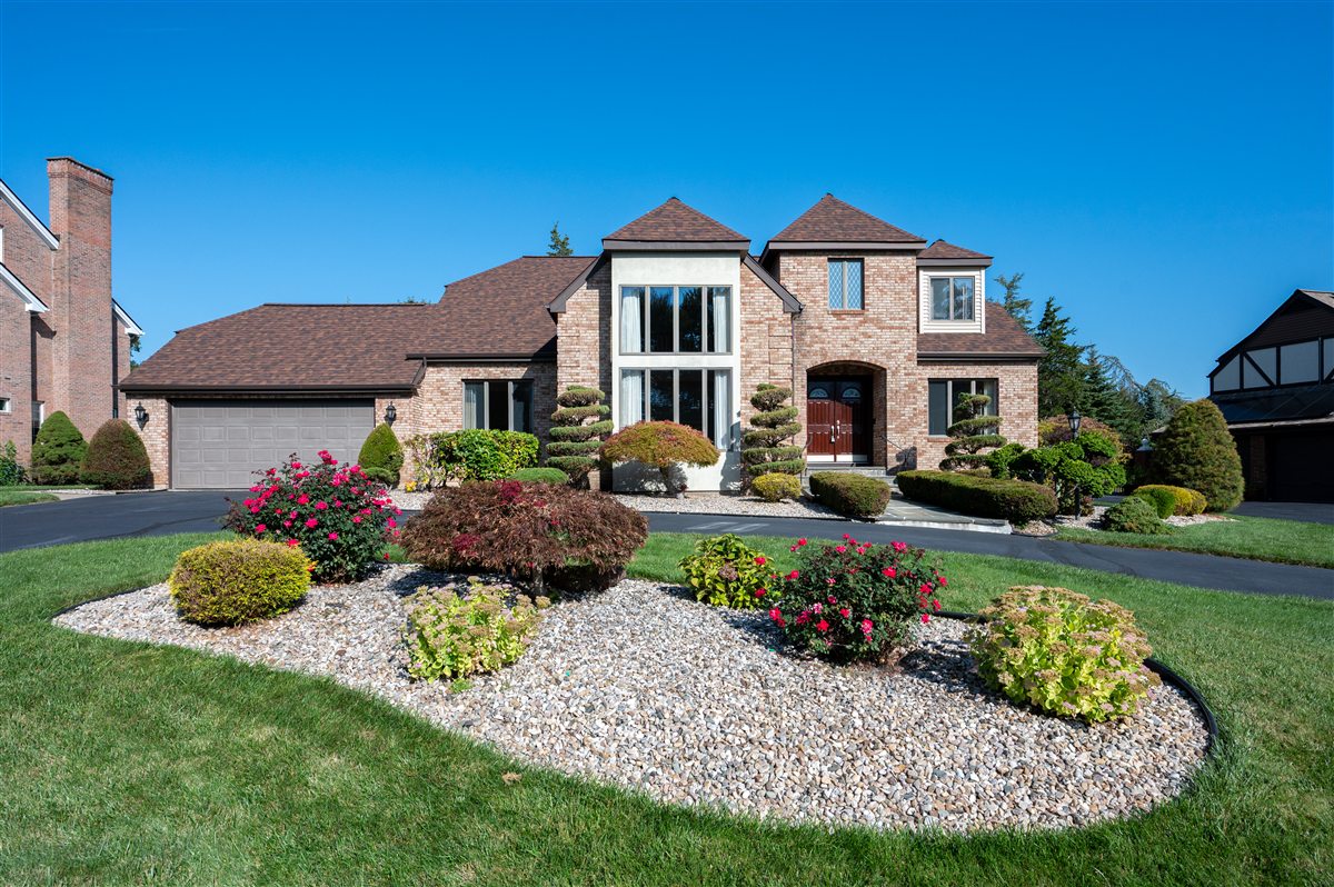 Original daytime exterior photograph of a brick home with sculpted shrubs and a curved flower bed