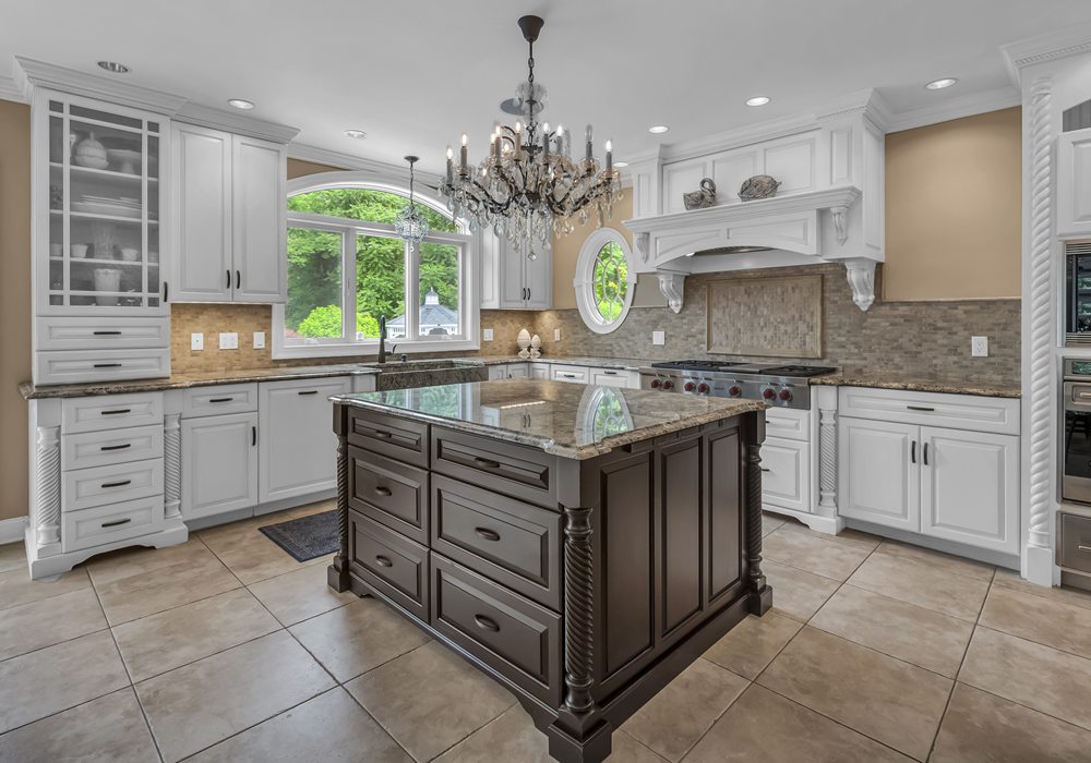 Traditional kitchen with a dark wood island, crystal chandelier, white cabinetry and an arched window