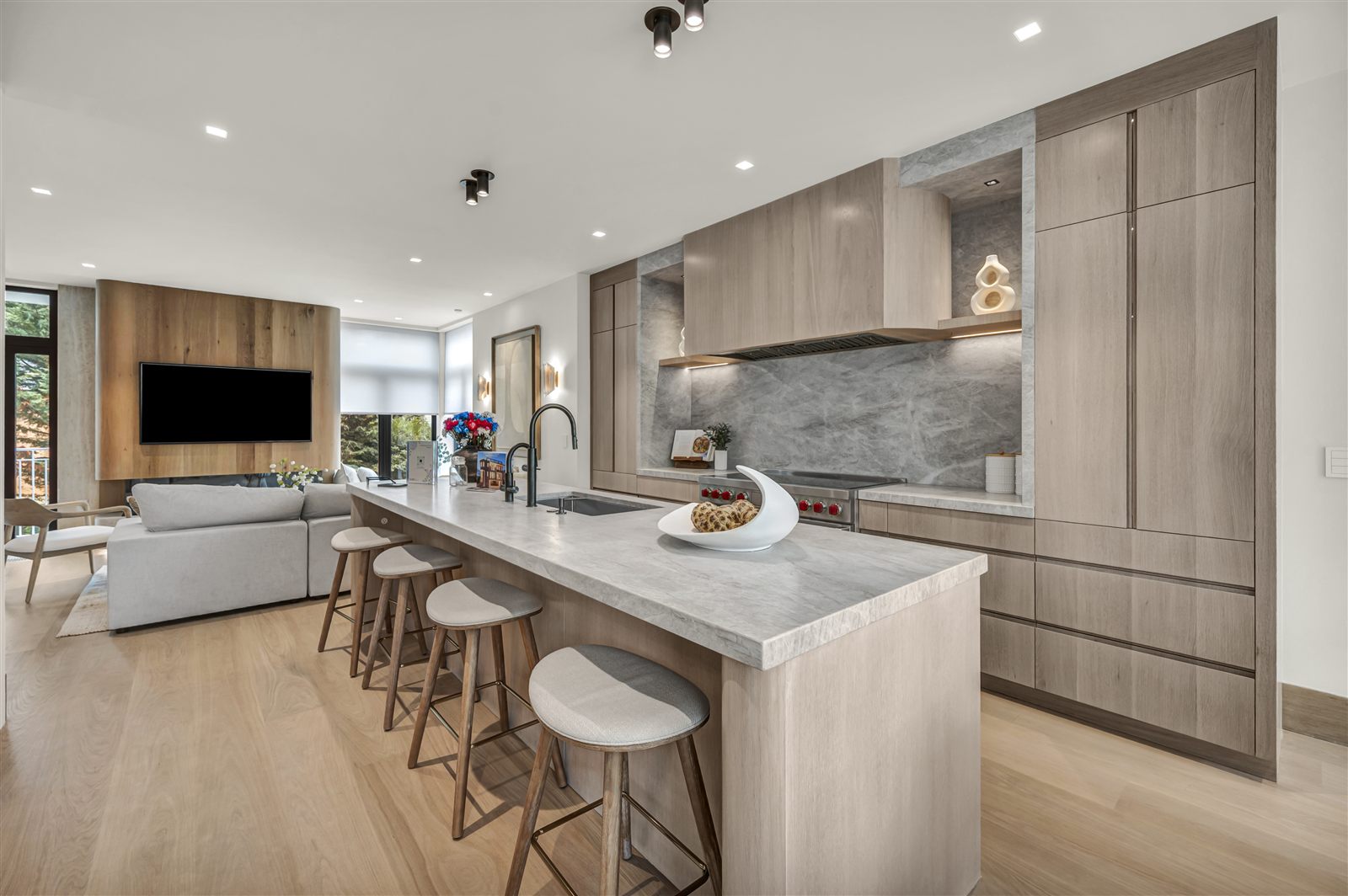 Modern kitchen with warm wood cabinetry, stone island and an adjoining living area