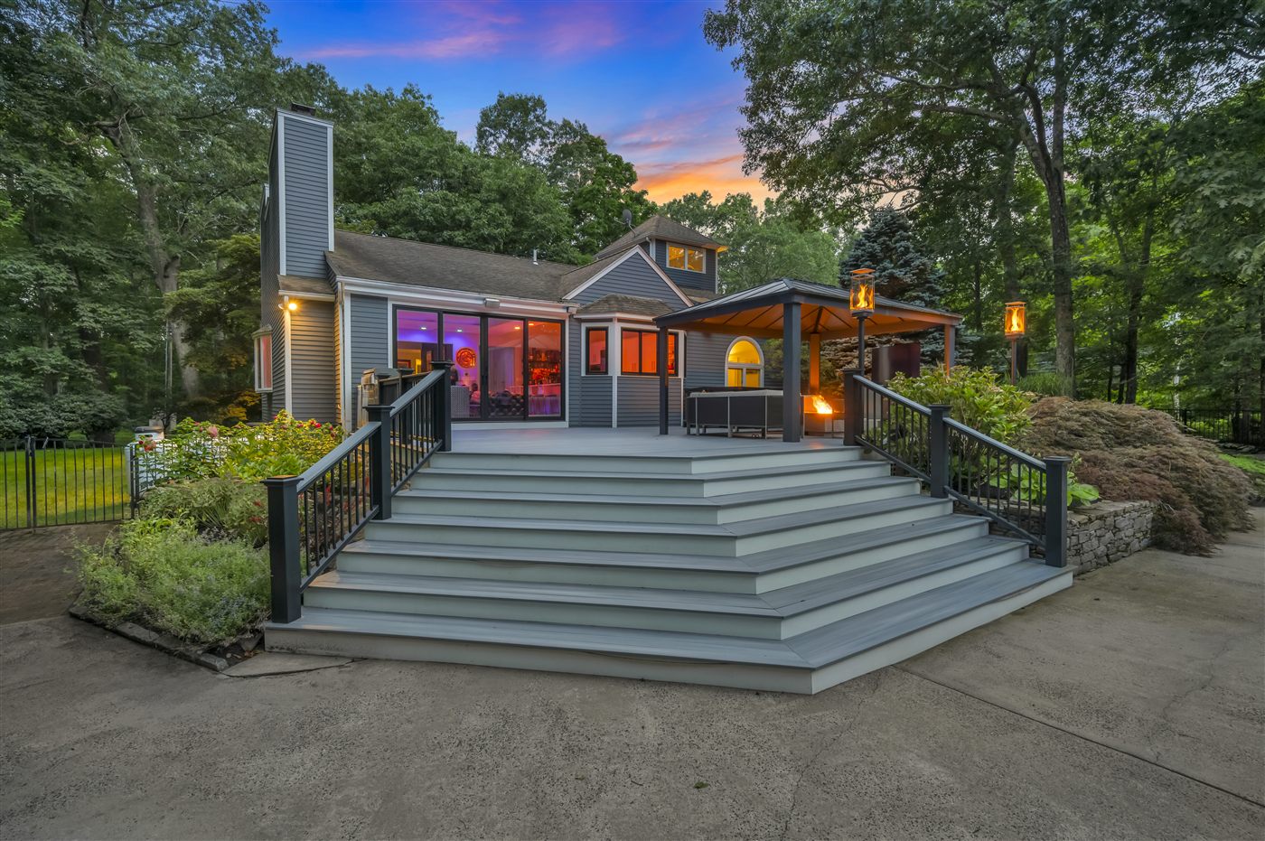 Home at twilight with a broad deck, glowing lanterns and a colorful evening sky